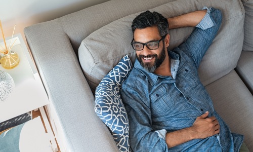 man sitting relaxing glasses sofa end table blue collar shirt black hair